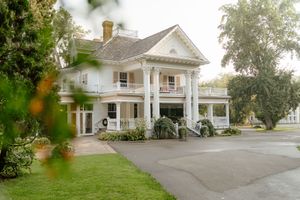 A beautiful white colonial style house with wrap-around porch and circular driveway viewed from multiple angles.