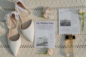 A collection of neutral-toned wedding details including shoes, invitations, and floral elements arranged on a textured surface.