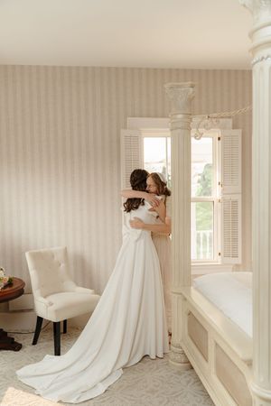 Elegant bridal moment in a light-filled room with striped wallpaper and flowing white wedding gown.