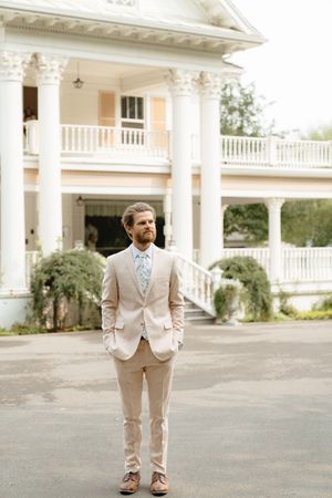 A person in a light beige suit stands in front of a grand white columned building.