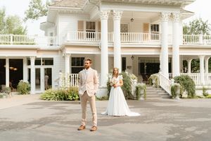 Elegant white mansion wedding venue with columns and couple standing in front.