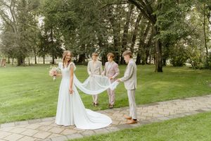 Wedding party members pose together on a lush green lawn with elegant white dresses and light colored suits.