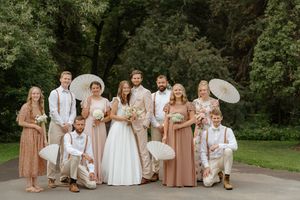 Wedding party group photo with people in white and blush pink attire on a garden path.