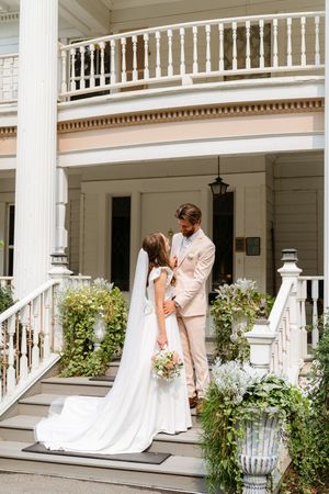 A wedding couple shares intimate moments on a classic white columned porch with elegant architectural details.