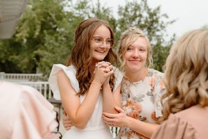Bridesmaids in blush pink dresses share joyful laughter during outdoor wedding photos.