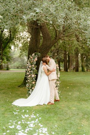 Romantic wedding couple shares intimate moments under blooming trees in a lush garden setting.