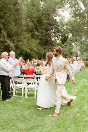 Wedding guests celebrating on a grassy lawn with white chairs during an outdoor reception.
