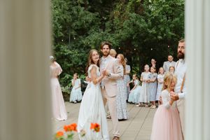 Wedding party in white and blush dresses gather outdoors for formal group photos on stone pathway.