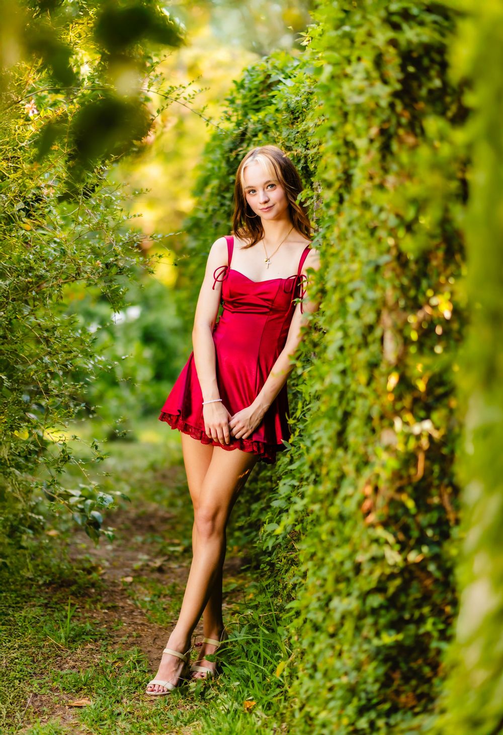 A red dress contrasts beautifully with lush green foliage in an outdoor portrait session.