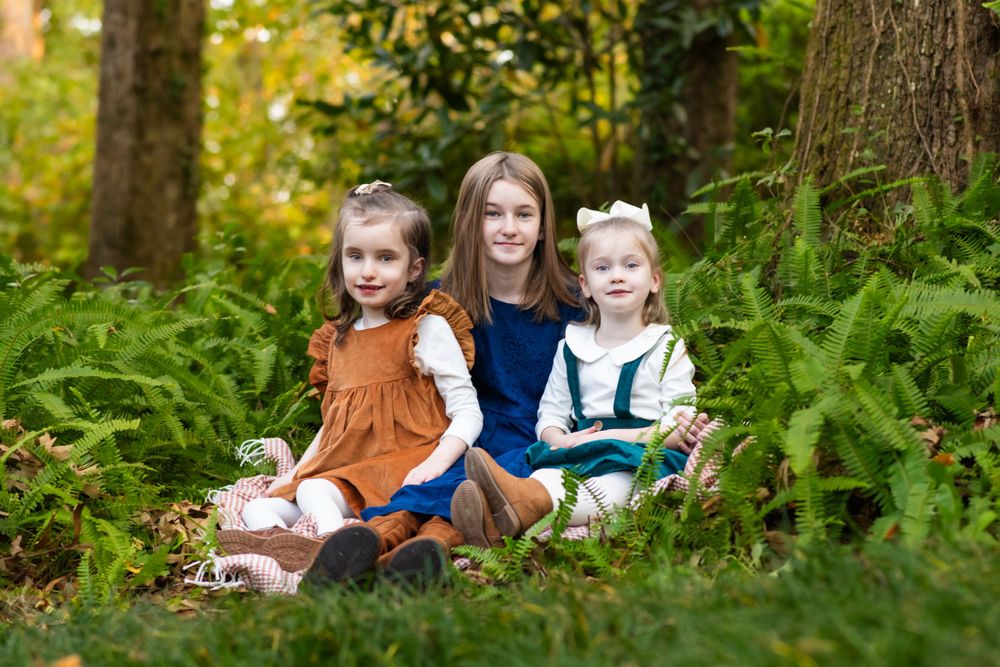 Three young sisters sitting among ferns in a forest, capturing a joyful and natural family moment.