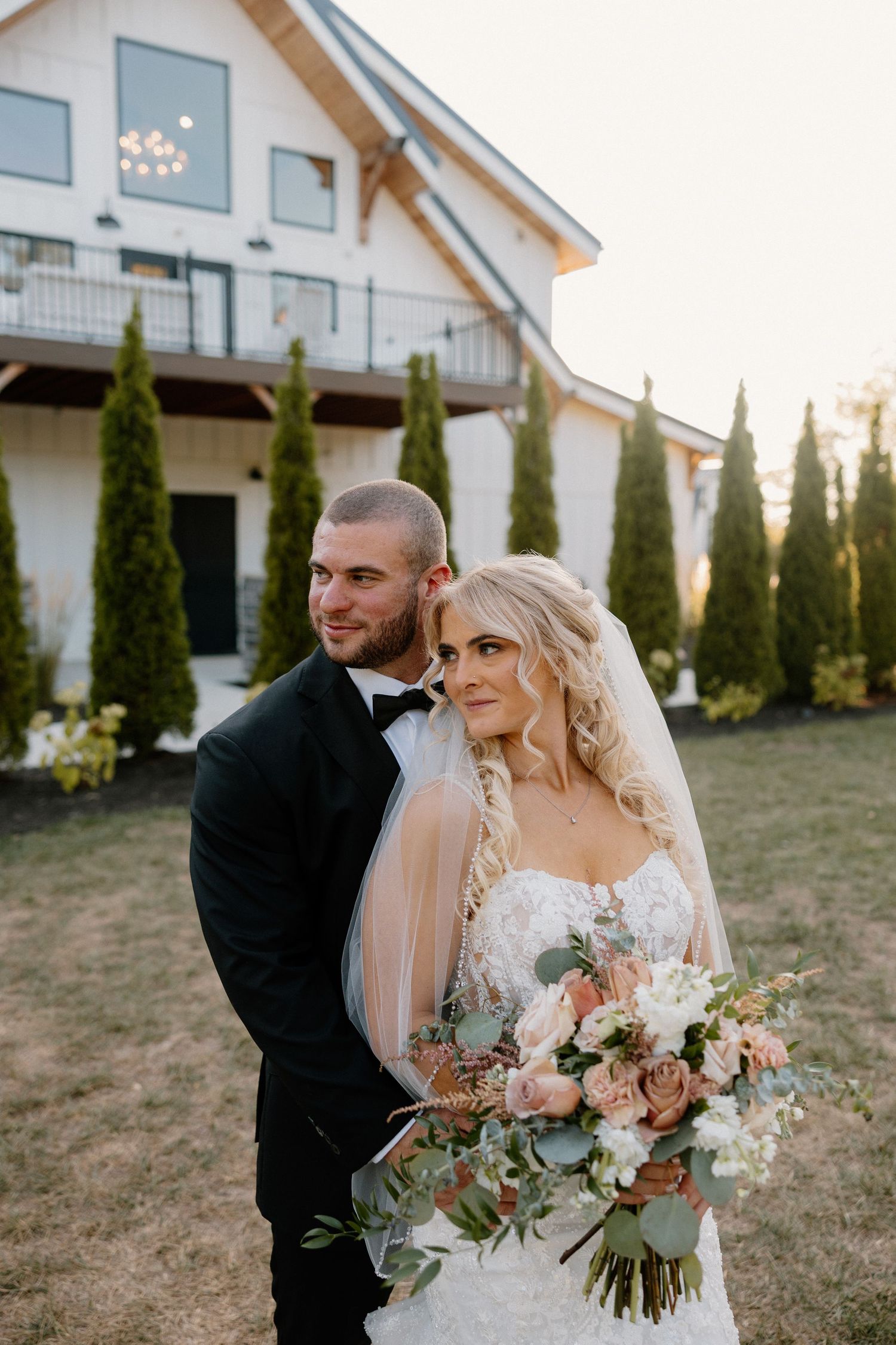 Wedding couple walks along pathway toward building with Reverie sign and manicured lawn.