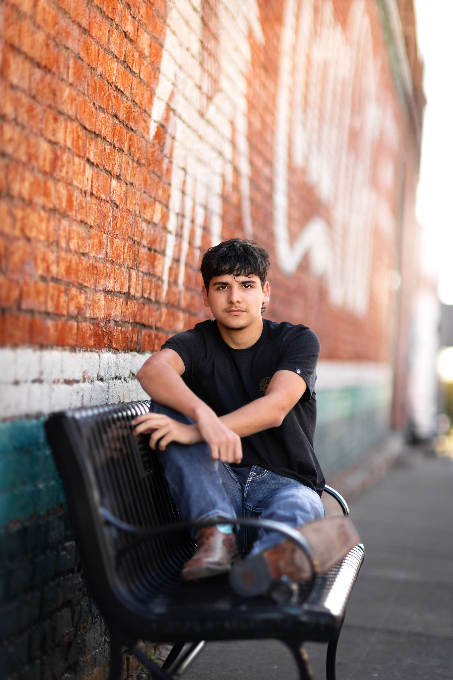 Person relaxing on a black bench against rustic brick wall.