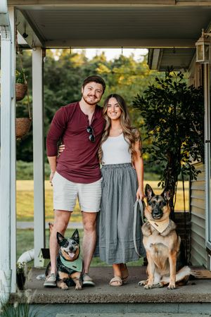 Two German Shepherd dogs sit on a front porch with their family during a casual portrait session.