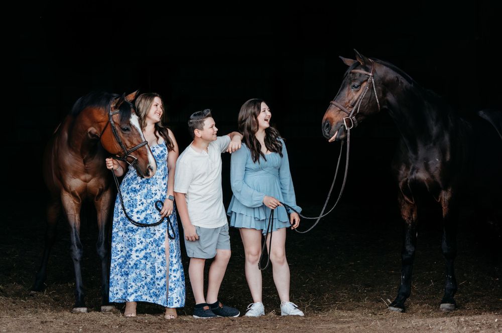 Group of people in blue dresses standing near horses at night.