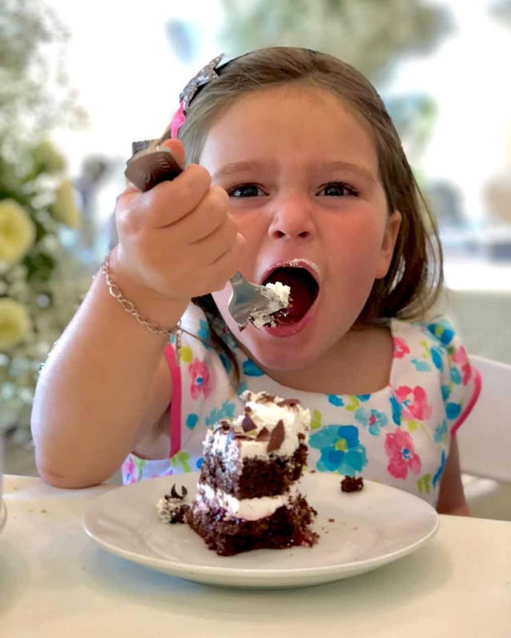 Young girl looking at camera while taking a bite of cake
