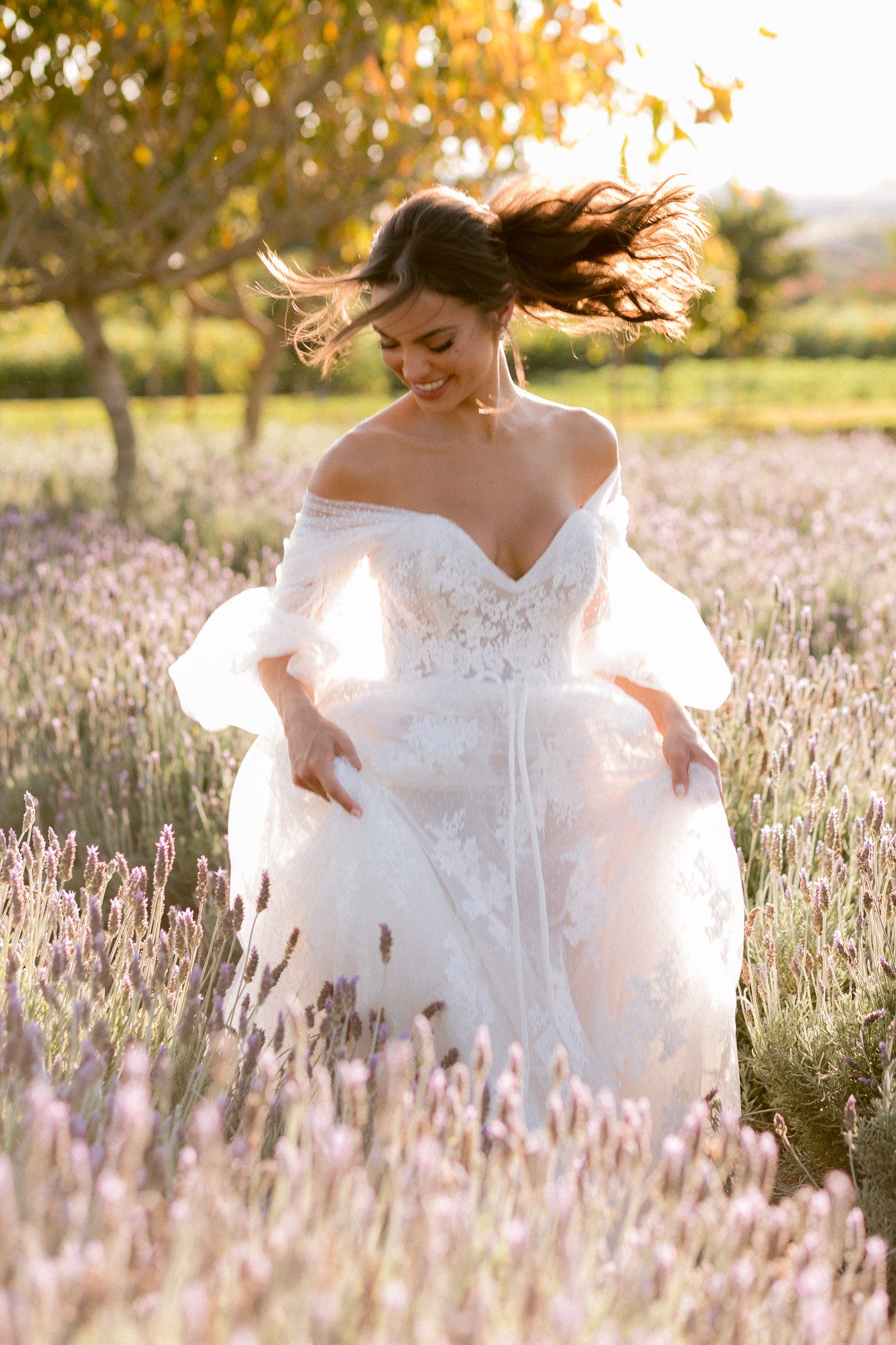 Bride in white gown sitting in field of tall grass during golden hour.
