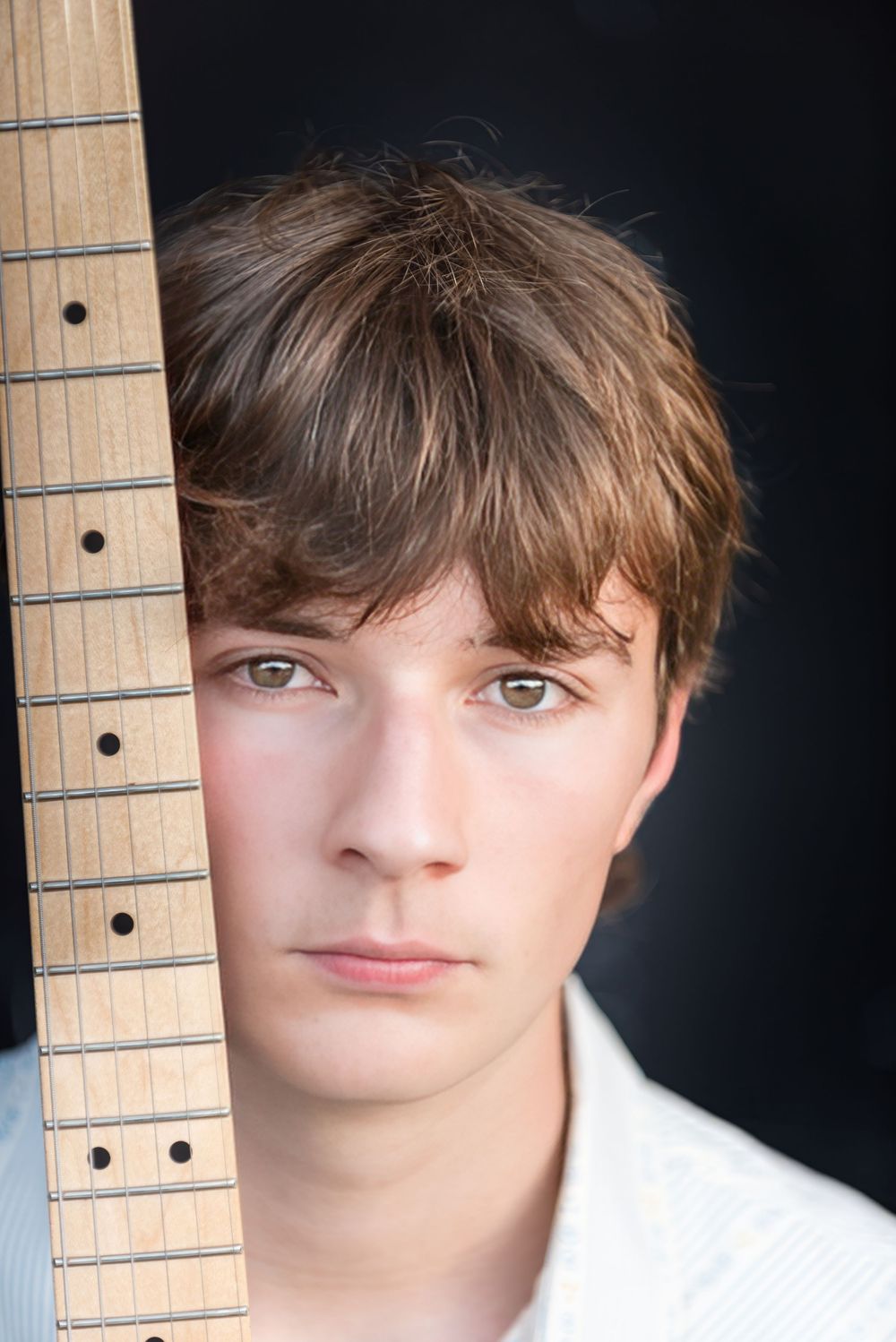 closeup of senior boy with blue eyes against guitar neck