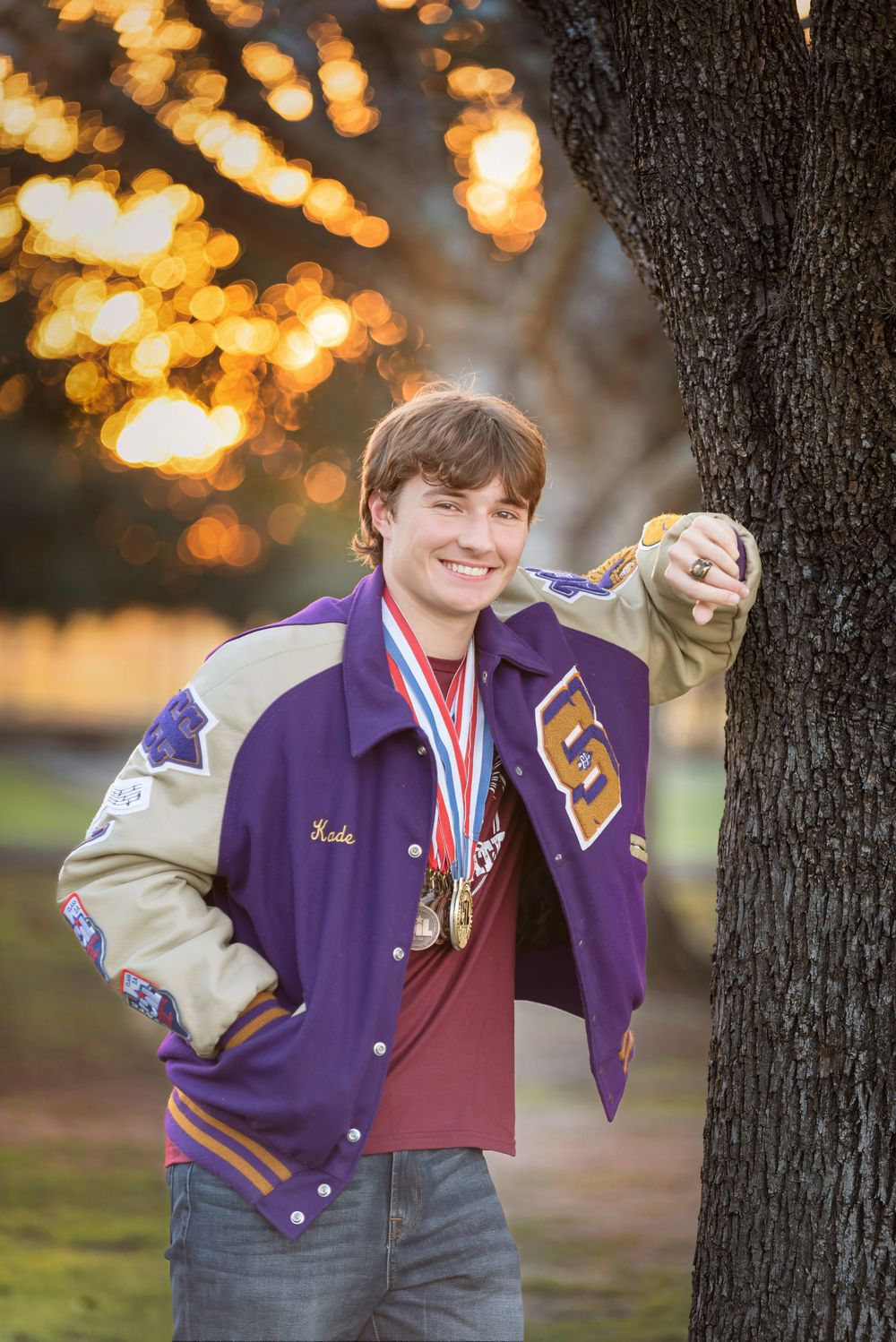 Senior boy smiling against tree wearing letterman