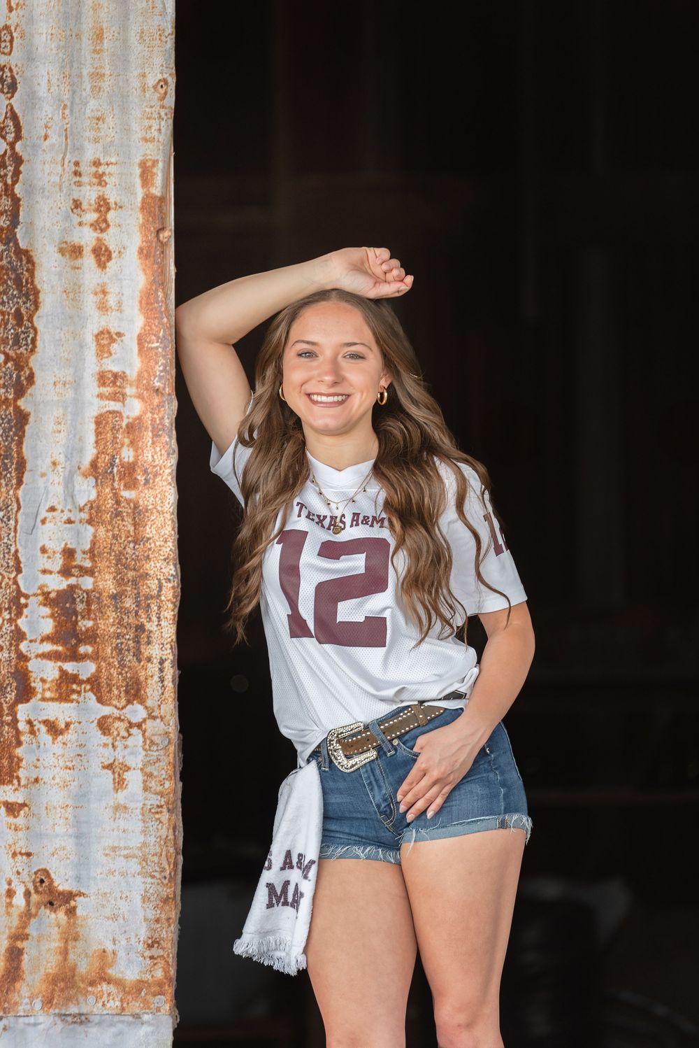 Senior girl smiling against door frame wearing aggie jersey and 12th man towel