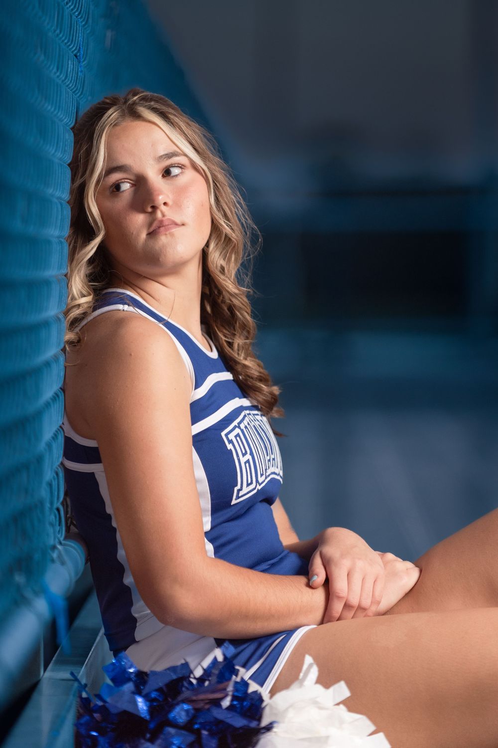 senior cheerleader wearing uniform at stadium at night looking pensive