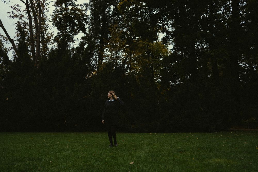 Verspieltes Vintage Portrait einer jungen Frau im schwarzen Pullover und Rock auf einer Wiese stehend im Großen Garten Dresden