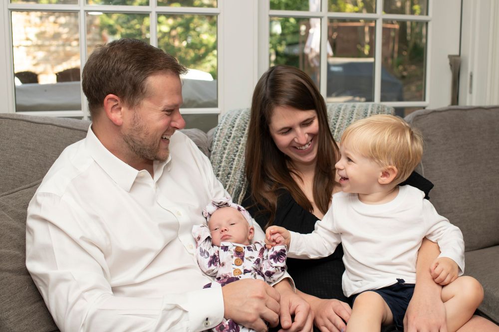Family shares joyful moment on grey couch while bonding with newborn baby.