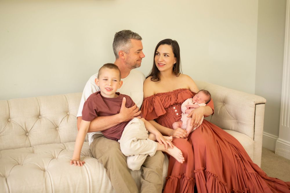 Family portrait on beige couch with children in warm-toned casual clothing.