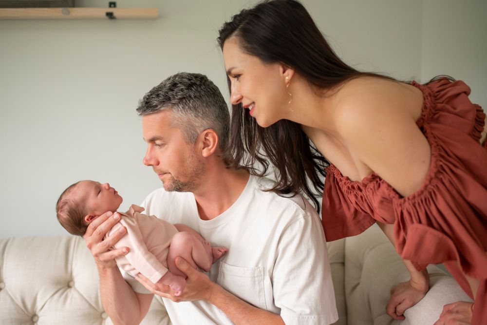 Tender moment with a newborn baby being cradled on a couch while wearing white.