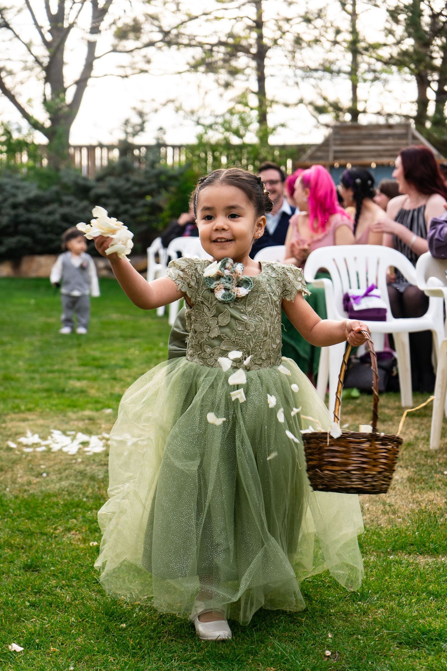 A romantic spring wedding moment with a flower girl in a green dress throwing petals from a brown basket.