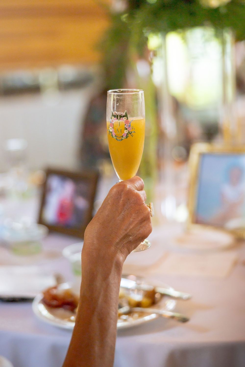 A hand raising a champagne flute filled with orange mimosa at an elegant wedding reception.
