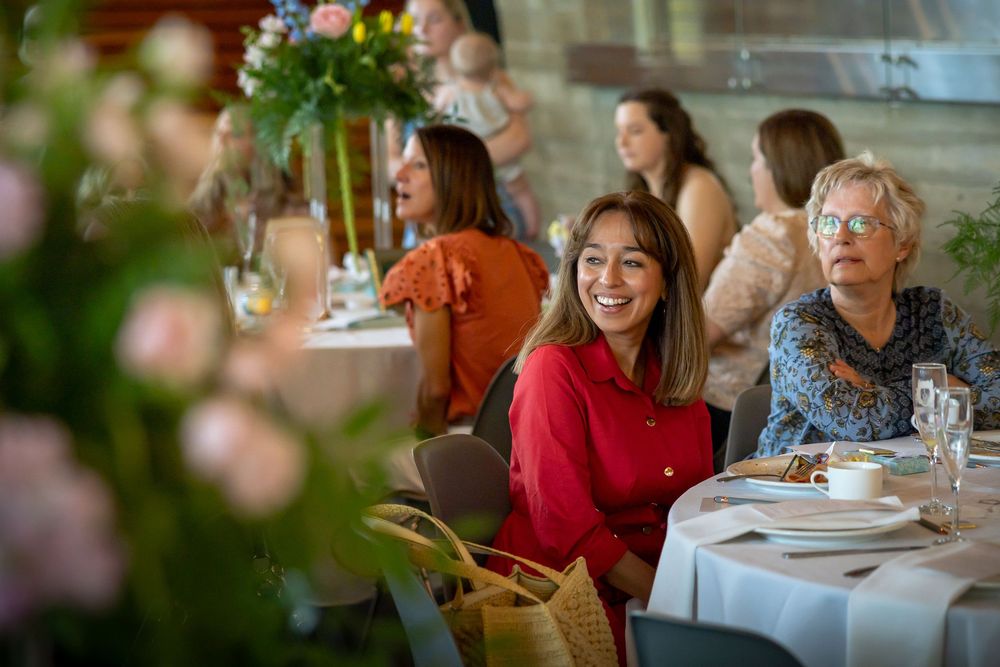 Women smiling and laughing together at elegantly set tables during a social dining event indoors.