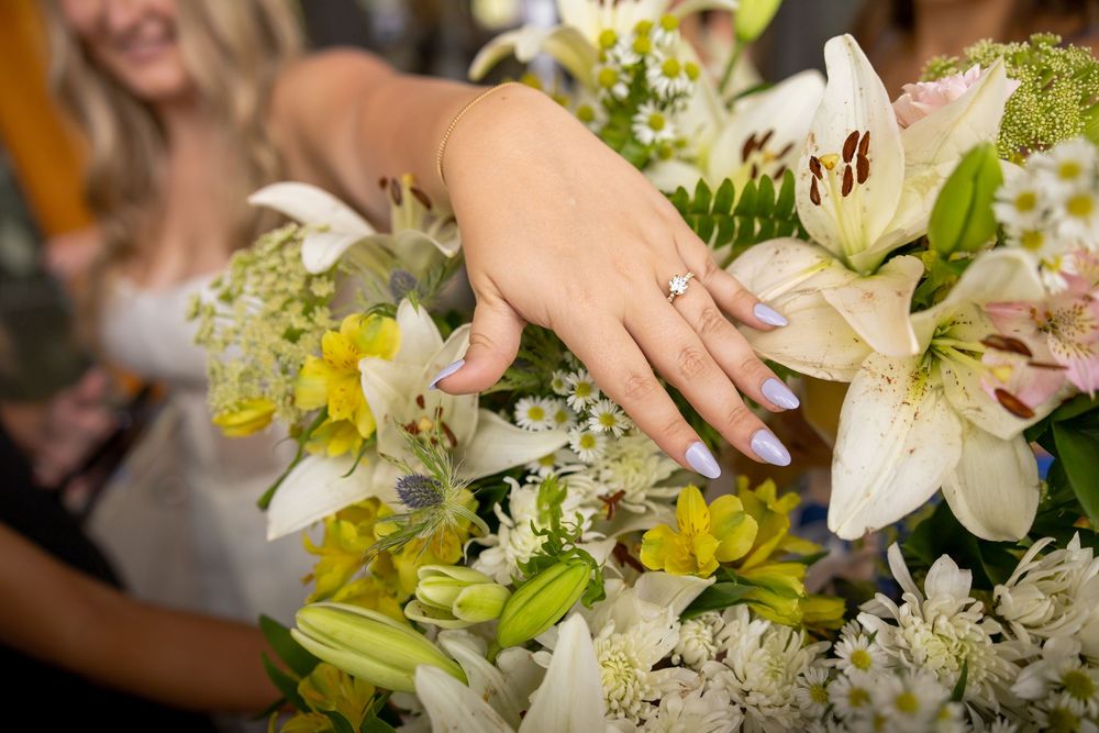 Close-up of bride's hand with diamond engagement ring resting on white lily bouquet.