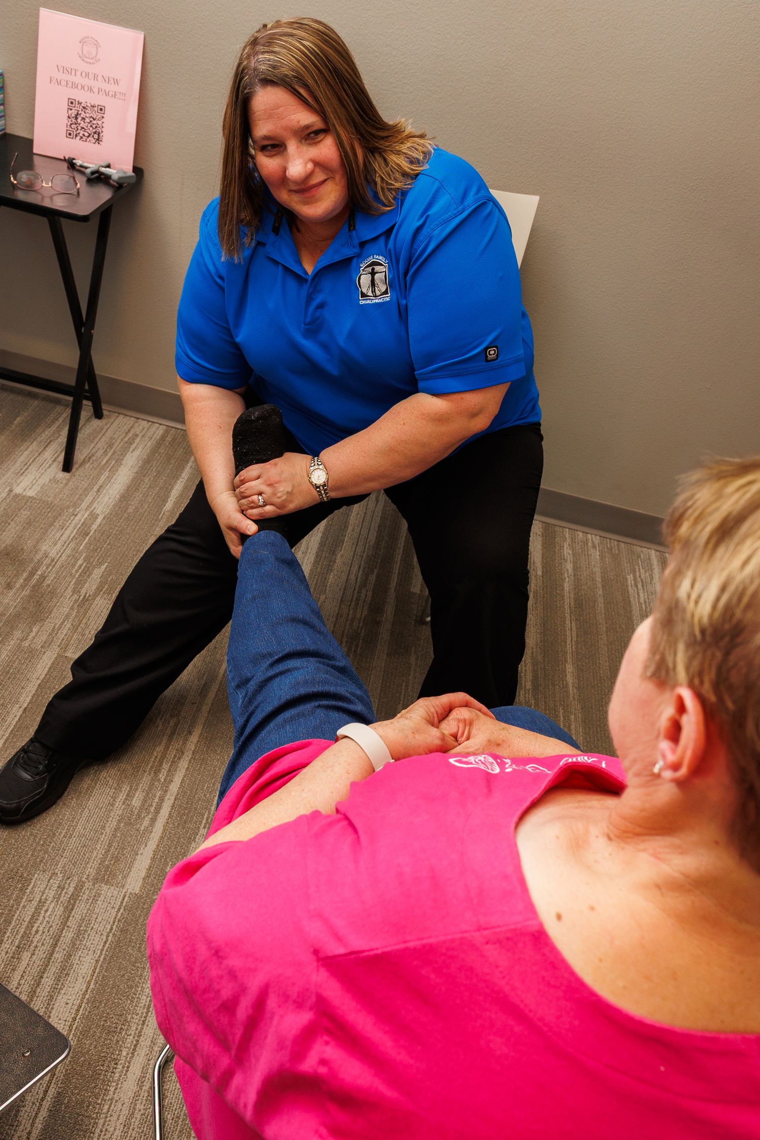 Physical therapist in blue polo shirt examining patient's leg during treatment session on gray floor.