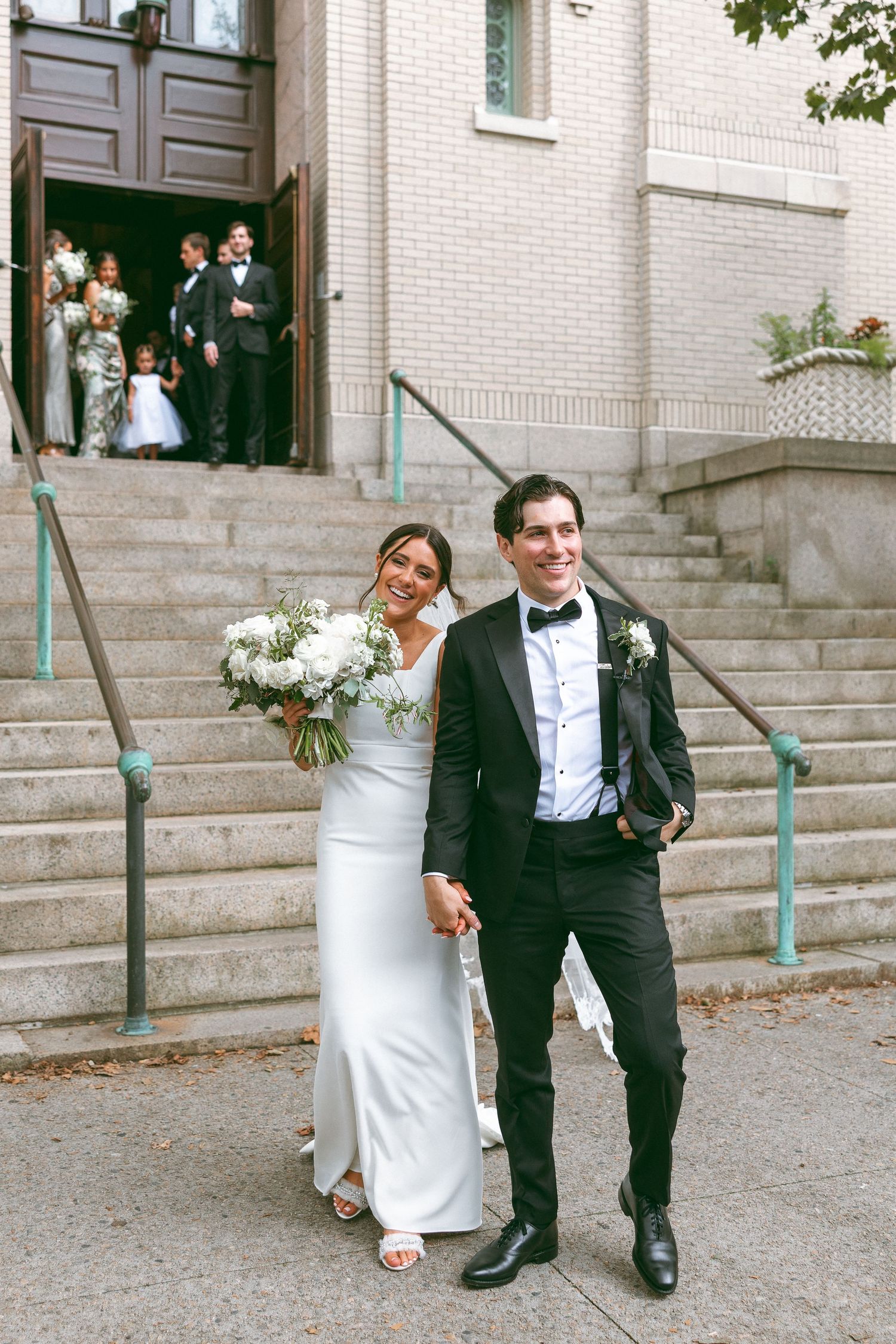 Wedding couple descending white stone steps outside a brick building.