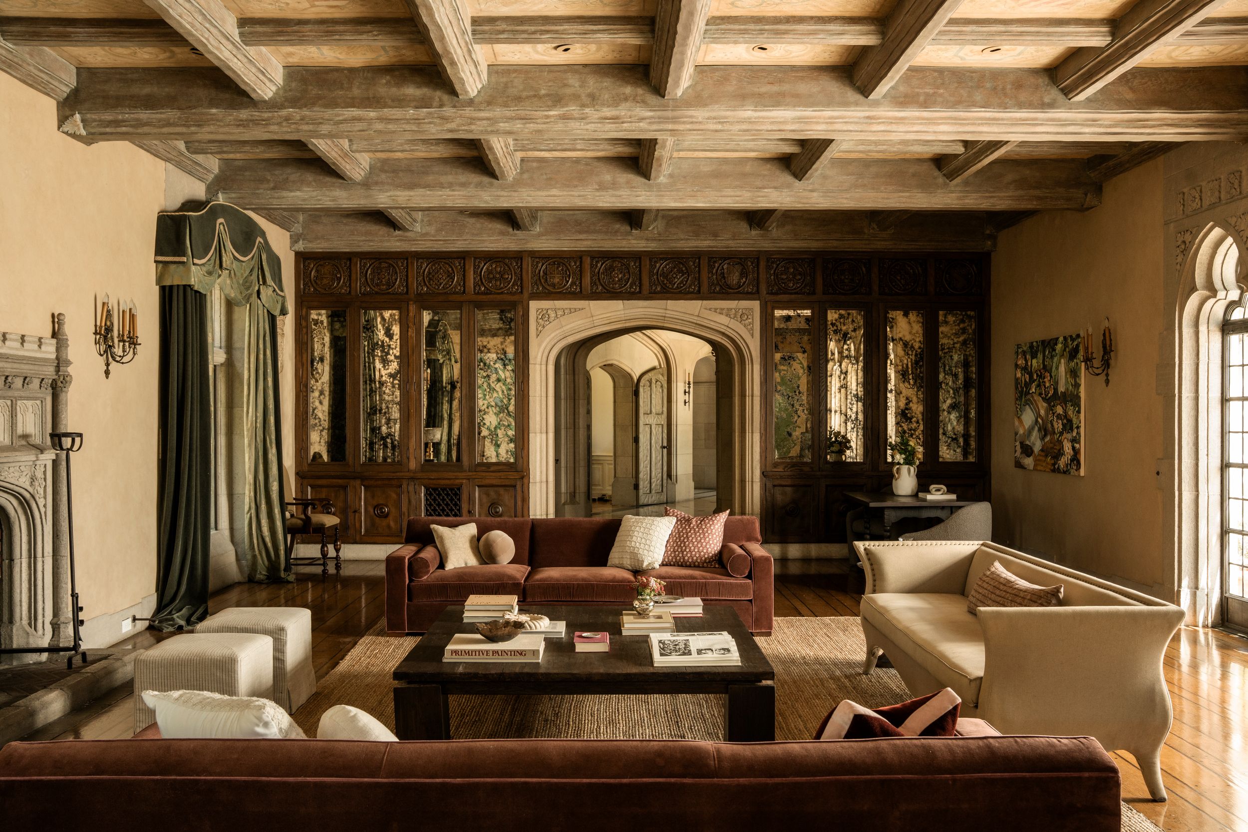Elegant traditional living room with rustic wood beam ceiling, arched doorway, rich brown leather sofas, and ornate wall paneling.