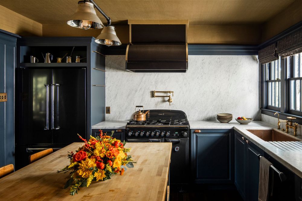 Vintage dark blue kitchen with wood countertop and colorful floral arrangement on island.