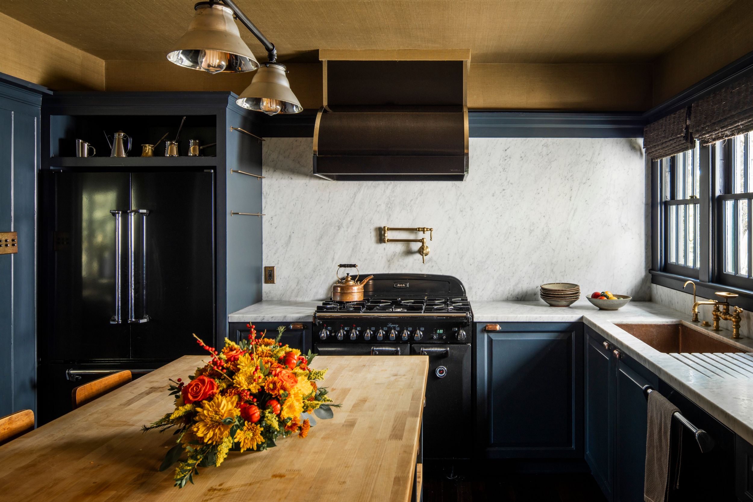 Vintage dark blue kitchen with wood countertop and colorful floral arrangement on island.