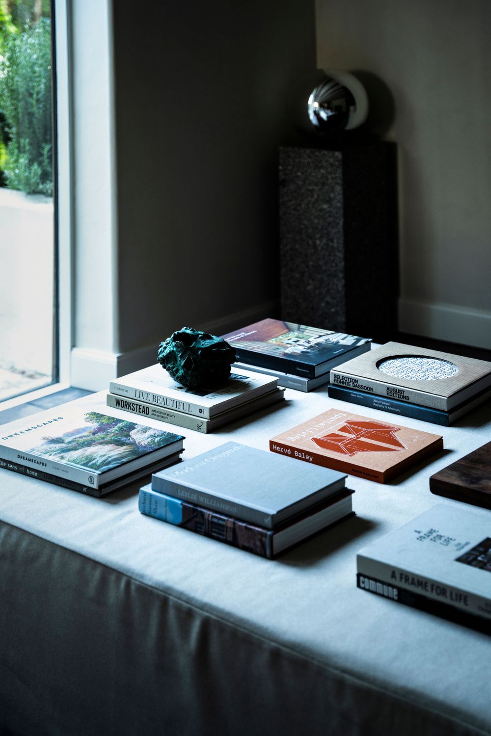 A collection of books and reading materials arranged on a white surface near a window with a decorative black sphere.