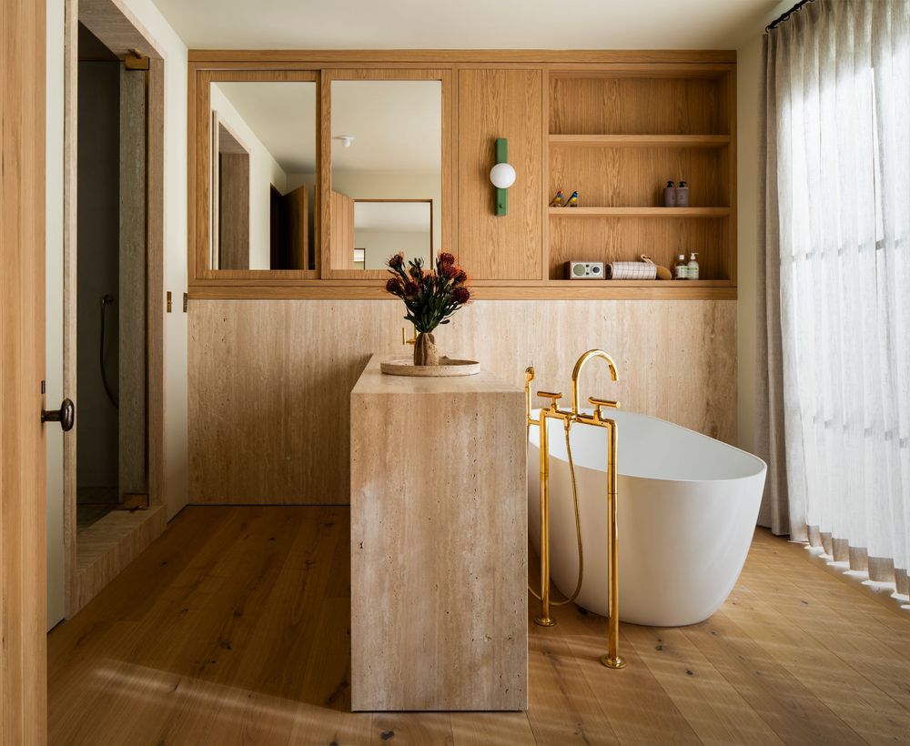 Modern minimalist bathroom with wood paneled walls, freestanding white tub, and brass fixtures in a luxurious setting.