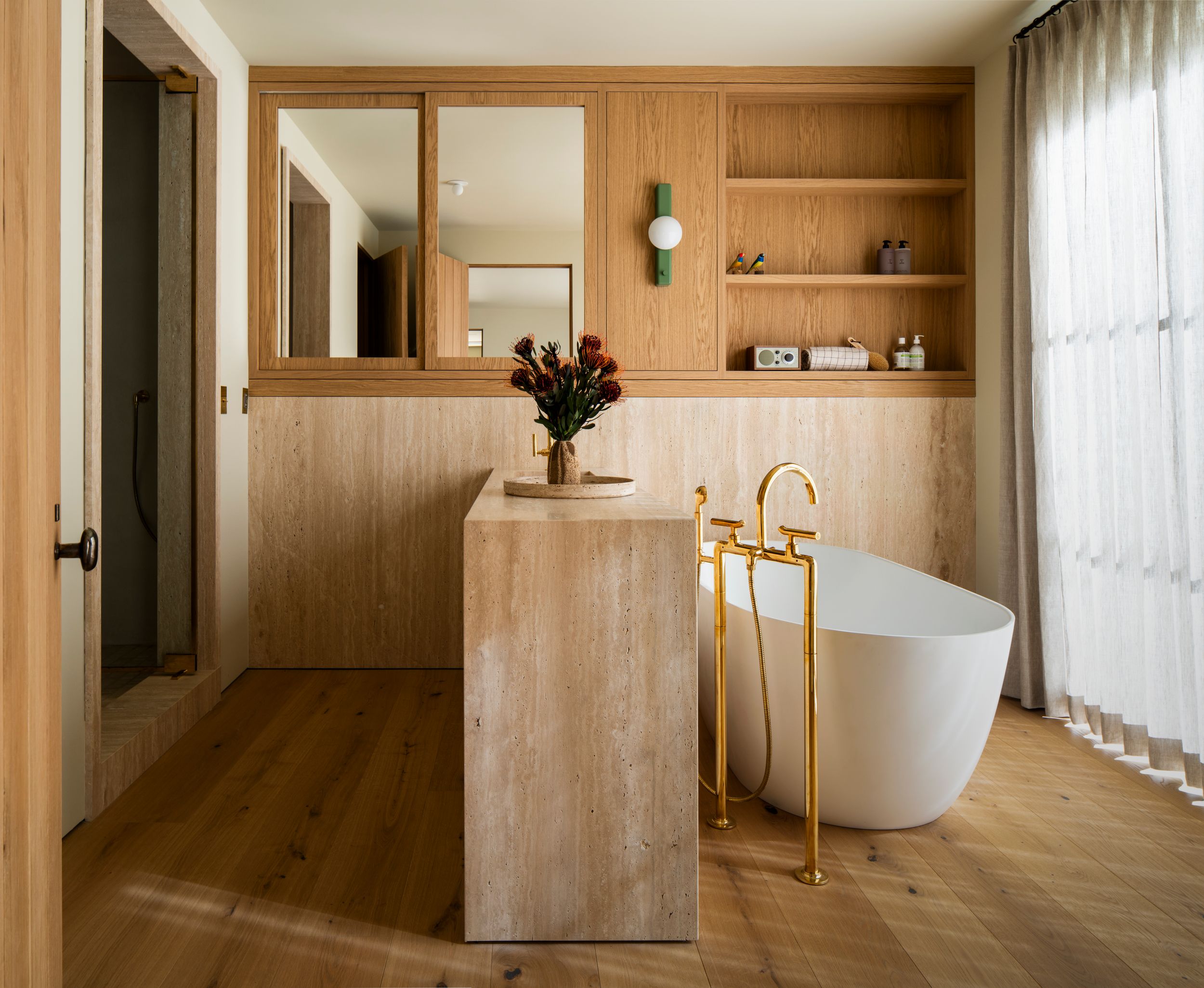 Modern minimalist bathroom with wood paneled walls, freestanding white tub, and brass fixtures in a luxurious setting.