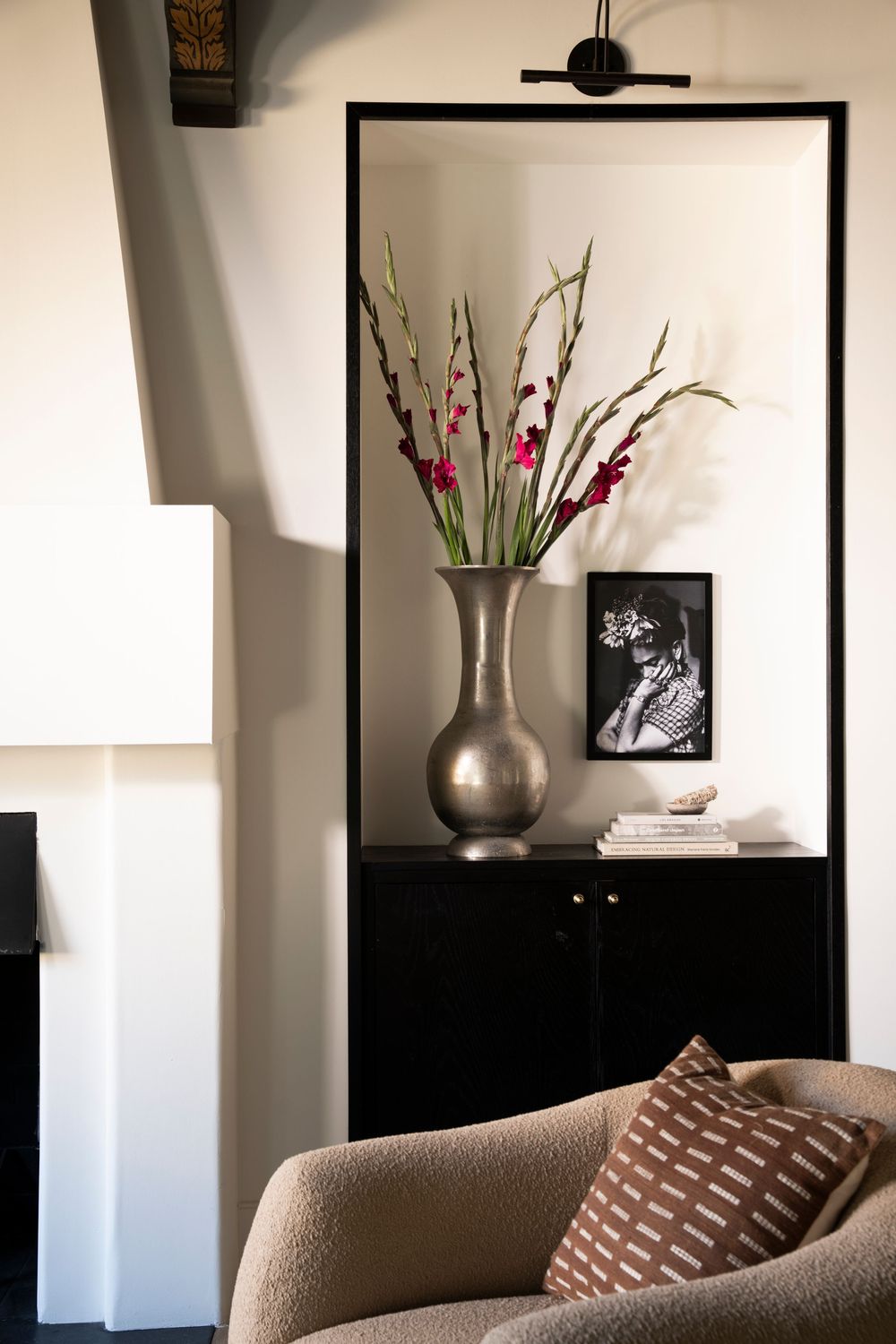 Modern living room interior with silver vase and flowers against black framed artwork and beige sofa.