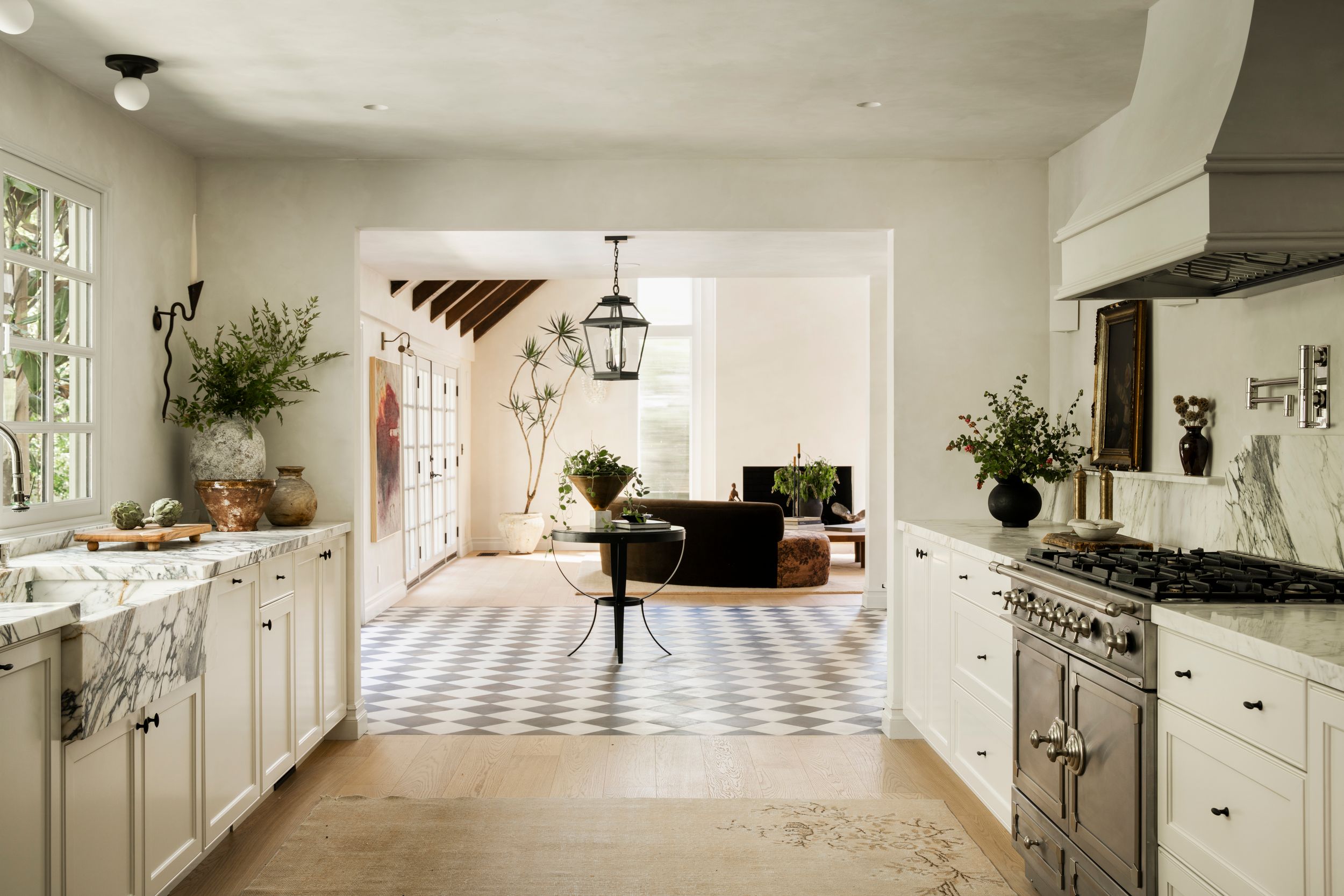 Bright white kitchen with checkered floor tiles opens to a cozy living room with pendant lighting and marble countertops.