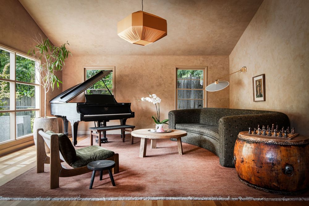 Elegant living room with grand piano, curved sofa, wooden coffee table, and warm terracotta walls in a cozy artistic space.