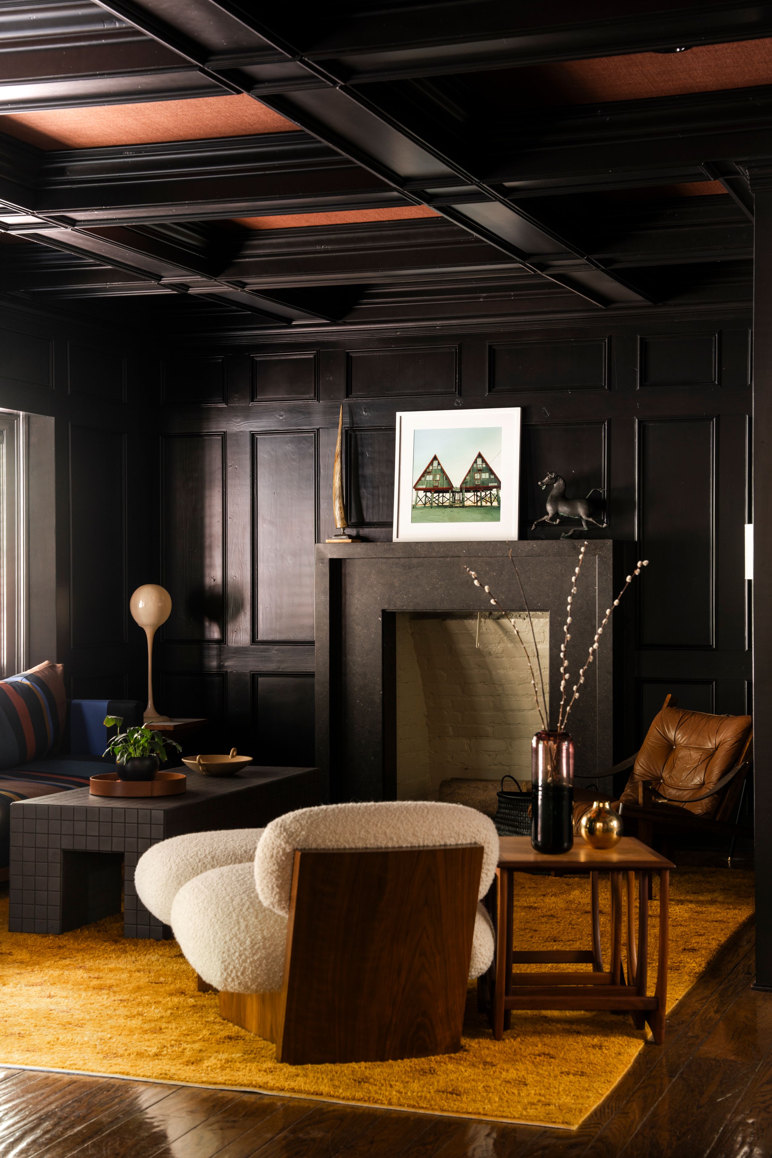 Moody living room with curved sofa, yellow area rug, and black paneled walls.