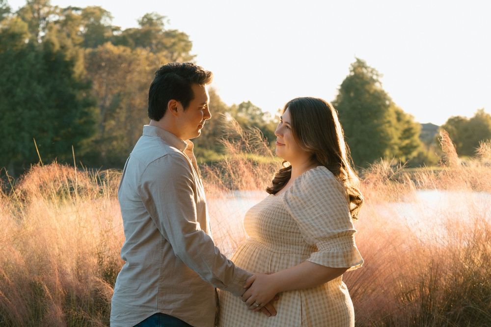 Couple sharing a tender moment in a golden field during a maternity photo session at sunset.