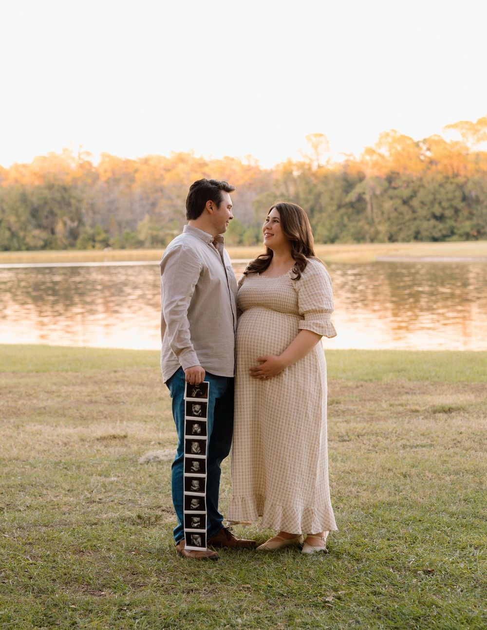 Couple sharing a tender moment during golden hour maternity photoshoot by a serene lake.