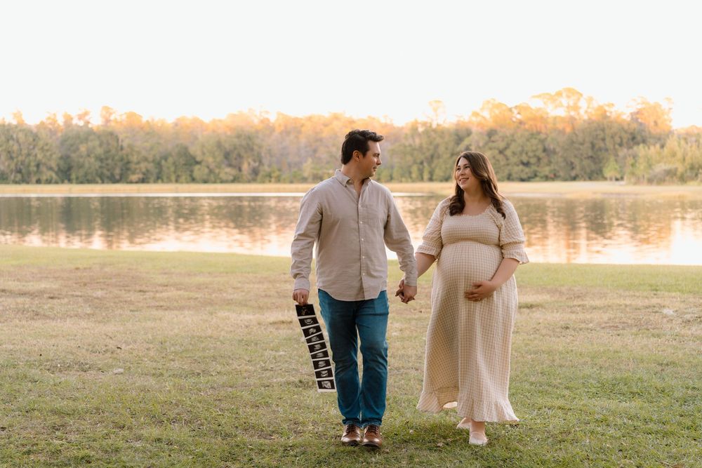 Pregnant couple walking hand in hand by a serene lake during golden hour maternity photoshoot.
