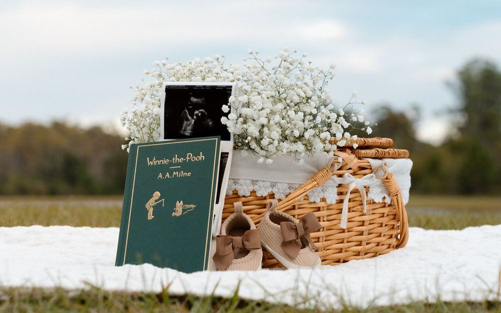 Winnie the Pooh book, wicker basket, and baby's breath flowers arranged on white blanket outdoors.