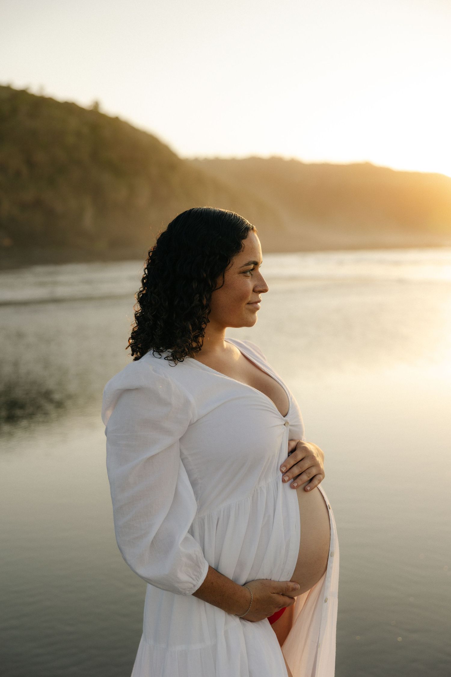 Ethereal maternity portrait in a forest setting with flowing white lace gown.