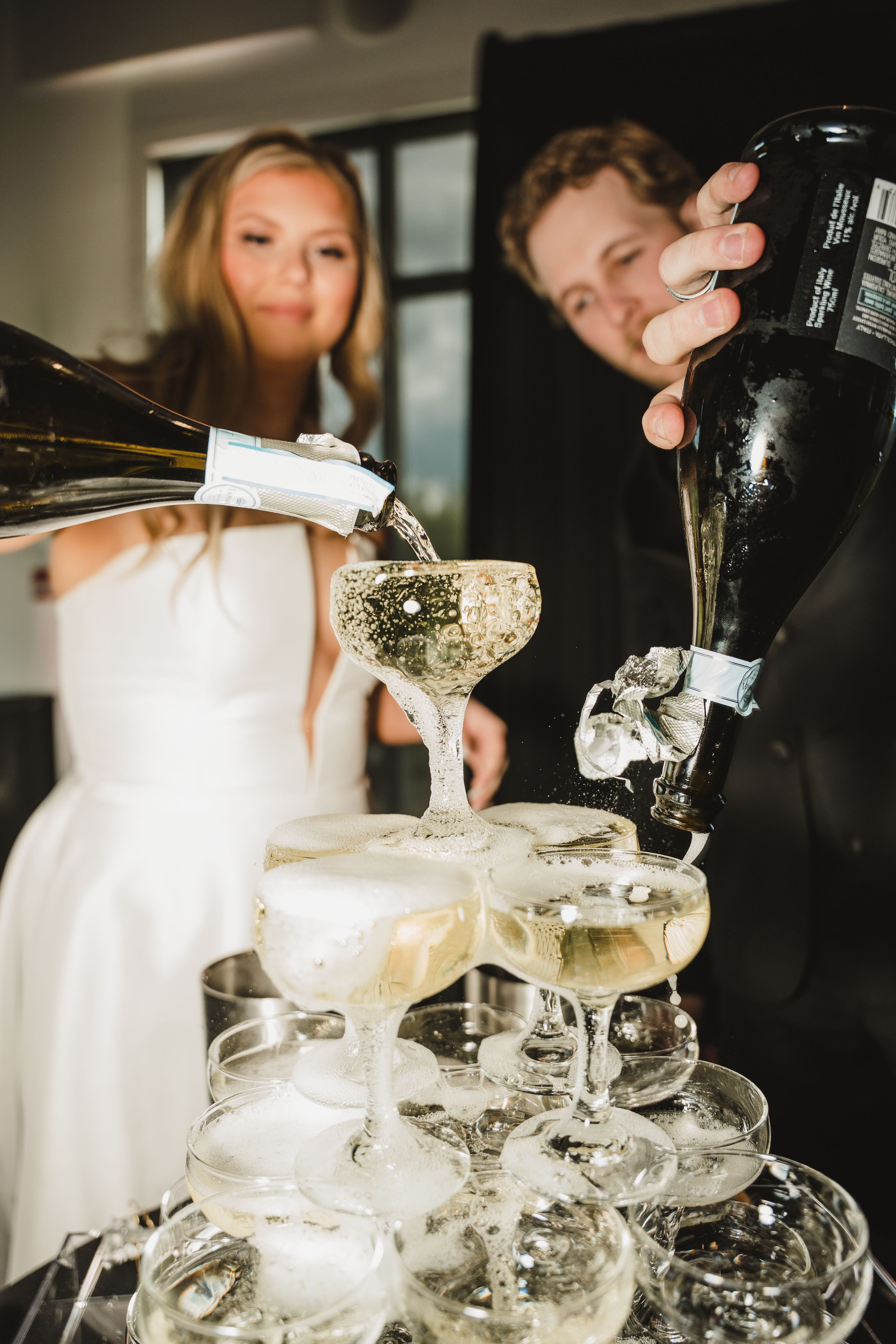Champagne being poured into a tower of vintage coupe glasses during an elegant wedding celebration.